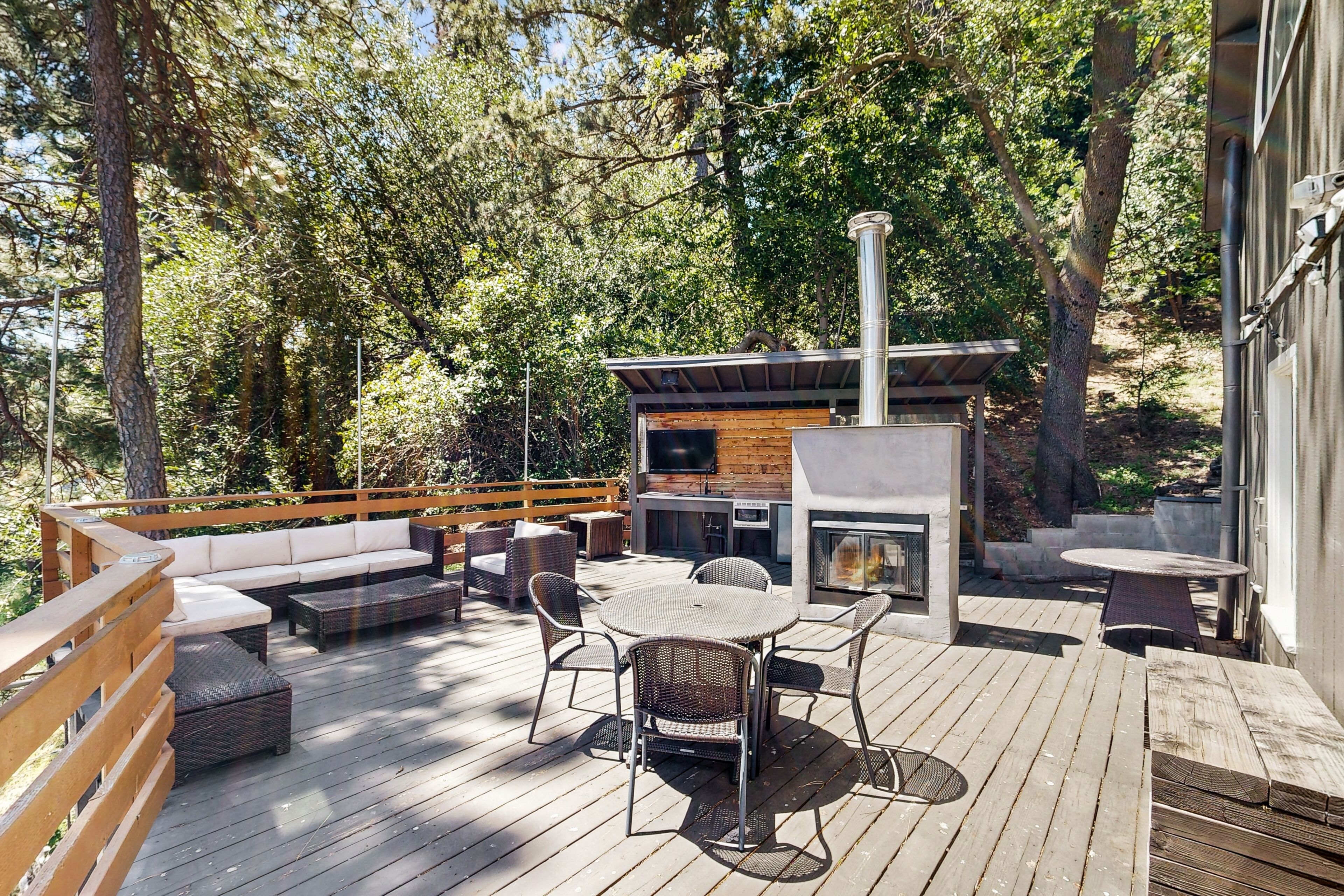 Eine Holzterrasse mit Gartenmöbeln, einem Grillbereich und einem Steinkamin.