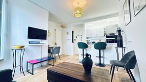 Ein modernes Wohnzimmer mit Fernseher, Sitzgelegenheiten, Küchenzeile und Essbereich.