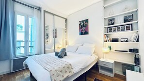 Ein Hotelzimmer mit einem Bett, Nachttischen, einem Bücherregal und einem großen Fenster mit Vorhängen.