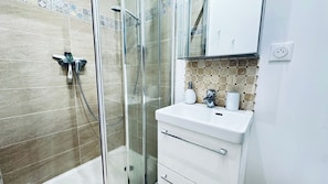 Un baño con cabina de ducha de vidrio, un lavabo blanco y un salpicadero de azulejos.