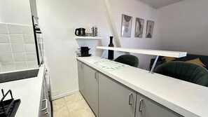 Eine Küche mit weißer Arbeitsplatte, grauen Schränken, einer Kaffeemaschine, einem Wasserkocher und einer kleinen Ablage mit Dekoration.