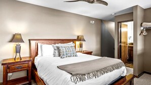 A bedroom with a bed, two bedside tables, a ceiling fan, and a door leading to a bathroom.