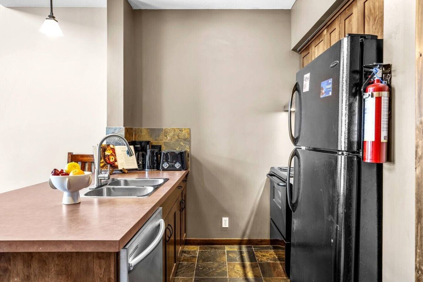 A compact kitchen with a sink, a toaster, a refrigerator, and a fire extinguisher mounted on the wall.