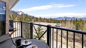 A balcony with a table, chairs, and a view of snow-capped mountains.