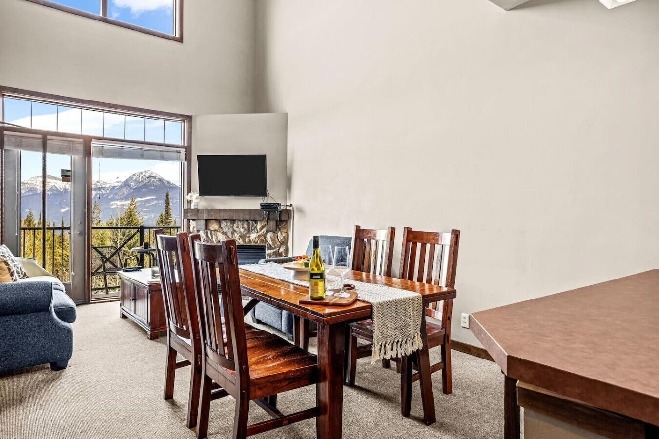 A dining area with a table, chairs, a TV, and a view of mountains.