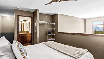 Une chambre à coucher comprenant un lit, un ventilateur de plafond, une étagère intégrée, une fenêtre donnant sur la montagne, ainsi qu’une salle de bain avec un miroir et un lavabo.