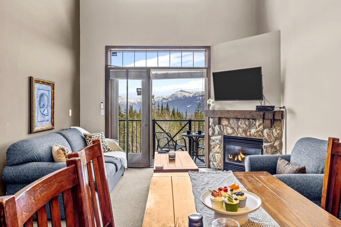 A living room with a fireplace, a sofa, a dining table, and a balcony with a mountain view.