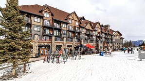 A multi-story hotel with ski rental services, a stone facade, and a ski slope in the background.