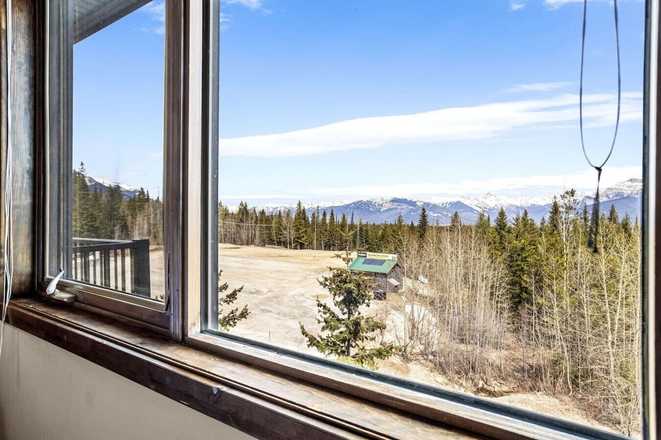 A window with a view of a mountainous landscape, a wooden deck, and a small building with solar panels.