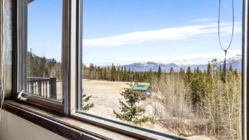A window with a view of a mountainous landscape, a wooden deck, and a small building with solar panels.