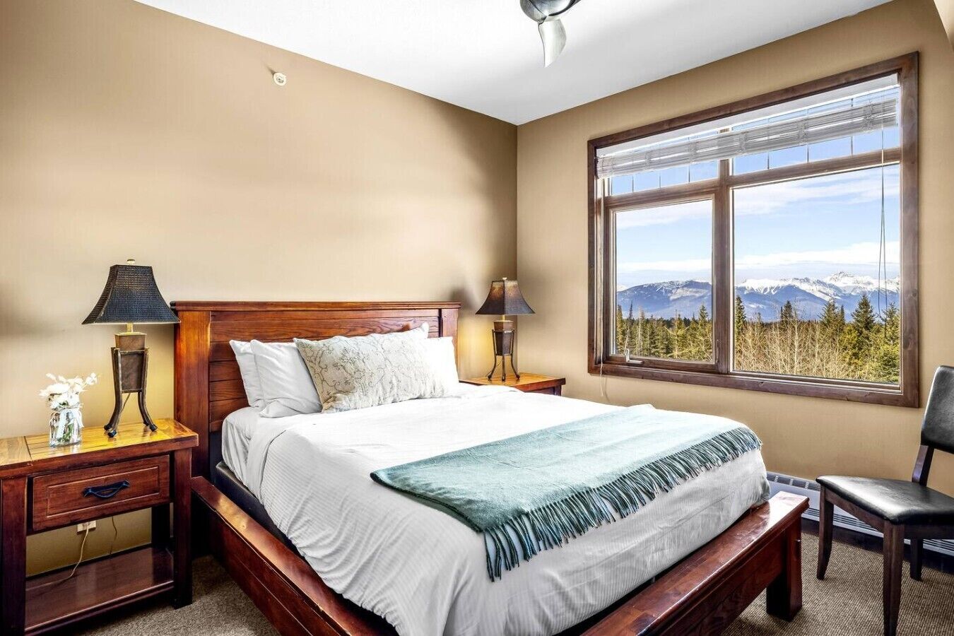 A bedroom with a bed, two bedside tables, a nightstand, a chair, and a window with a mountain view.
