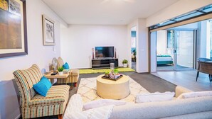Ein modernes Wohnzimmer mit Sofa, Couchtisch, Fernseher und einem Balkon mit Bett.