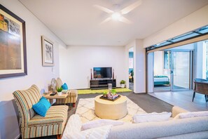 A modern living room with a sofa, a coffee table, a TV, and a balcony with a bed. - Luxury 2 BR | Pool Gym Parking Sydney CBD getaway (Camperdown)