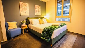 Ein Schlafzimmer mit einem Bett, einem Sessel, einem Nachttisch, einer Lampe und zwei an der Wand befestigten Kunstwerken.