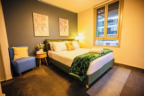 A bedroom with a bed, a chair, a bedside table, a lamp, and two wall-mounted artworks. - Luxury 2 BR | Pool Gym Parking Sydney CBD getaway (Camperdown)
