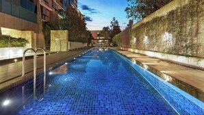 Ein Schwimmbecken mit Fliesenboden, umgeben von Gebäuden und einer Hecke.