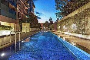 A swimming pool with a tiled floor, surrounded by buildings and a hedge. - Luxury 2 BR | Pool Gym Parking Sydney CBD getaway (Camperdown)