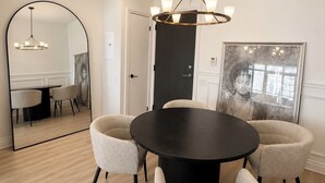Ein Essbereich mit einem runden Tisch, vier Stühlen, einer Kristallleuchter, einem großen Spiegel und einem gerahmten Kunstwerk an der Wand.