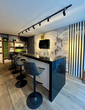 A modern kitchen with a bar area, bar stools, a flat-screen TV, and a cityscape mural on the wall. - Downtown Santiago Oasis: Rooftop Pool, Cowork Space & Sunset Balcony (Santiago)