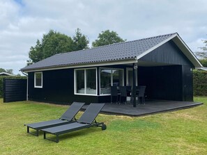 A black house with a covered patio, a dining table, and two lounge chairs. - 5 Star Holiday Home in Odder (Odder)