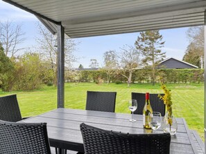 An outdoor patio with a table and chairs, a bottle of wine, and a vase with flowers. - 5 Star Holiday Home in Odder (Odder)