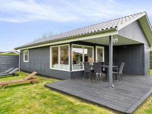 A covered outdoor patio with a table and chairs, a wooden deck, and a lawn. - 5 Star Holiday Home in Odder (Odder)
