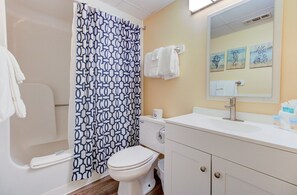 A bathroom with a shower curtain, toilet, sink, and mirror. - Oceanfront 1 Bedroom Condo in Carolina Beach 0808 (Carolina Beach)