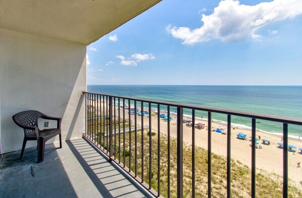 A balcony with a view of a beach, a chair, and a railing. - Oceanfront 1 Bedroom Condo in Carolina Beach 0808 (Carolina Beach)