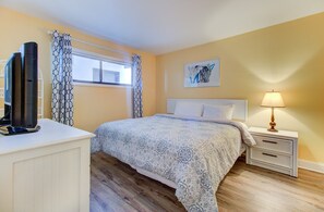 A bedroom with a bed, bedside table, lamp, and a TV on a stand. - Oceanfront 1 Bedroom Condo in Carolina Beach 0808 (Carolina Beach)