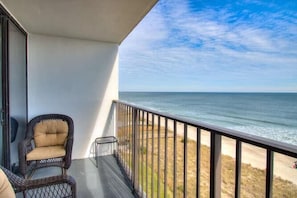 Un balcone con vista sull'oceano, una sedia in vimini e un tavolino.