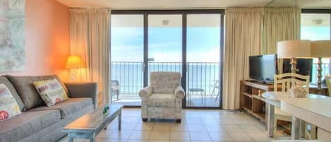 A living room with a sofa, armchair, TV, and a balcony with curtains.