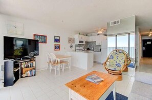 Ein modernes Wohnzimmer mit Fernseher, Bücherregal, Essbereich und einer Küche im Hintergrund.
