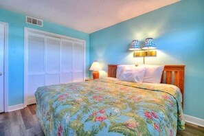 A bedroom with a bed, a nightstand, a lamp, and a closet. - Oceanfront paradise: 1BR condo with stunning views in Carolina Beach 0903 (Carolina Beach)