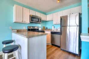 A kitchen with white cabinets, a stainless steel refrigerator, a microwave, and a stove. - Oceanfront paradise: 1BR condo with stunning views in Carolina Beach 0903 (Carolina Beach)
