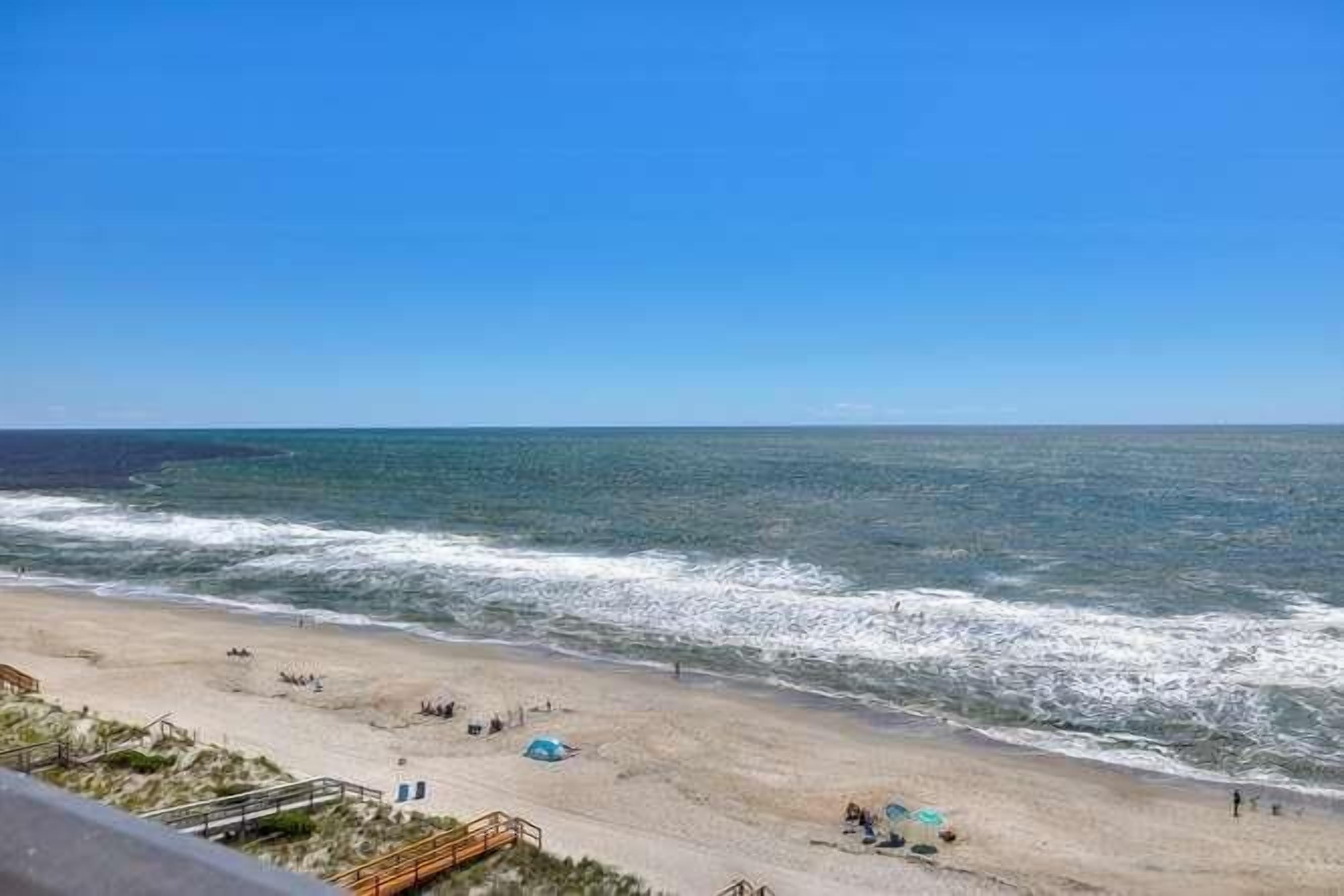 Ein Strand mit blauem Himmel, sandigem Ufer und einigen Zelten.