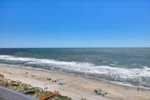A beach with a clear sky, sandy shore, and a few tents. - Oceanfront paradise: 1BR condo with stunning views in Carolina Beach 0903 (Carolina Beach)