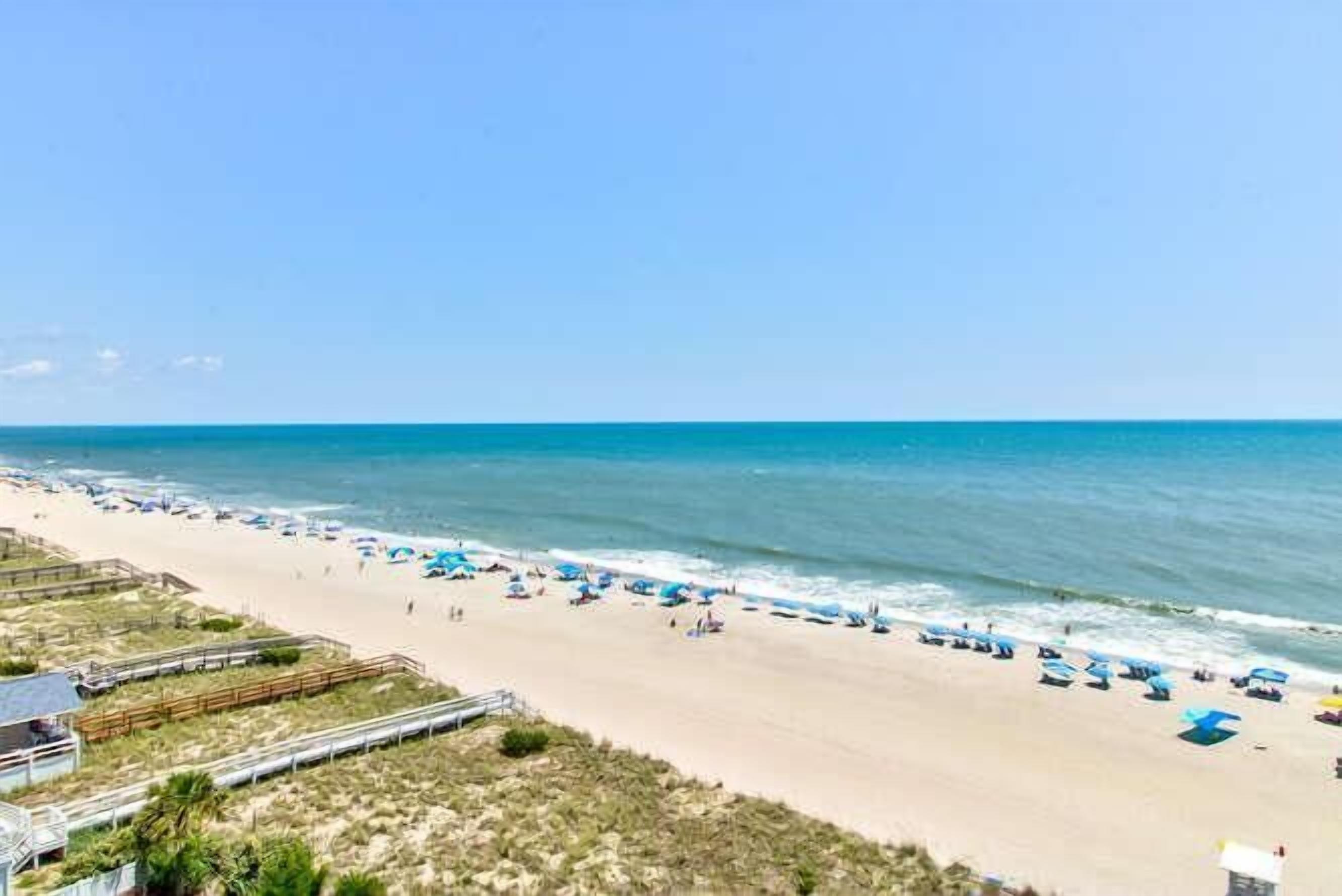 Ein Strand mit einer Holzpromenade, Strandstühlen und blauem Himmel.