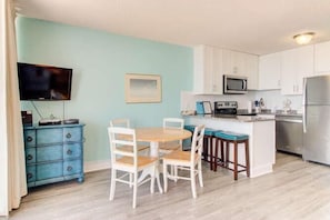 A compact kitchen with white cabinets, a microwave, a refrigerator, and a dining area with a table and chairs. - Oceanfront 1BR condo in Carolina Beach 0909 (Carolina Beach)