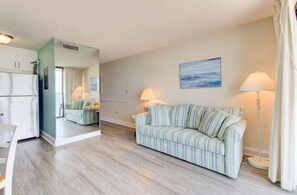A living room with a striped sofa, a lamp, and a painting on the wall. - Oceanfront 1BR condo in Carolina Beach 0909 (Carolina Beach)