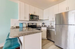A kitchen with white cabinets, a stainless steel refrigerator, a microwave, and a stove. - Oceanfront 1BR condo in Carolina Beach 0909 (Carolina Beach)