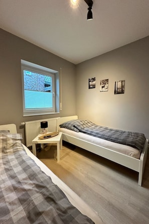 A bedroom with a single bed, a desk, a window with blinds, and three framed pictures on the wall. - FEWO „Am Stausee“ by Interhome (Friesoythe)