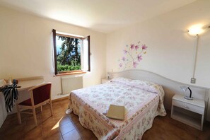 A bedroom with a bed, a desk, a chair, a nightstand, a lamp, and a window with a view of greenery. - Holiday flat with a view of the Bay of Val di Sogno (Malcesine)