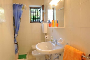 A bathroom with a white sink, a window with bars, a shower curtain, and a towel rack with an orange towel. - Holiday flat with a view of the Bay of Val di Sogno (Malcesine)