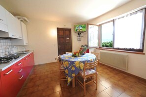 A kitchen with red cabinets, a gas stove, a dining table with a floral tablecloth, and a window with a view. - Holiday flat with a view of the Bay of Val di Sogno (Malcesine)