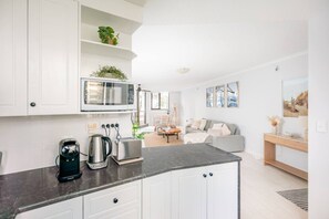 A modern kitchen with white cabinets, a built-in microwave, and a coffee maker. - Coastal Oasis | Sleeps 5 | Beach View + Pool & Gym (Surfers Paradise)