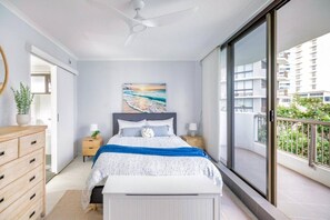 Ein Schlafzimmer mit Bett, Nachttischen, einem Fenster und einem Balkon.