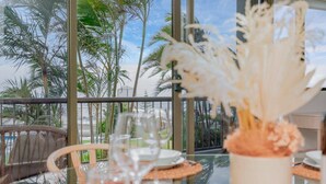 Una mesa de comedor con cristalería y una decoración, con vista a una playa con palmeras.