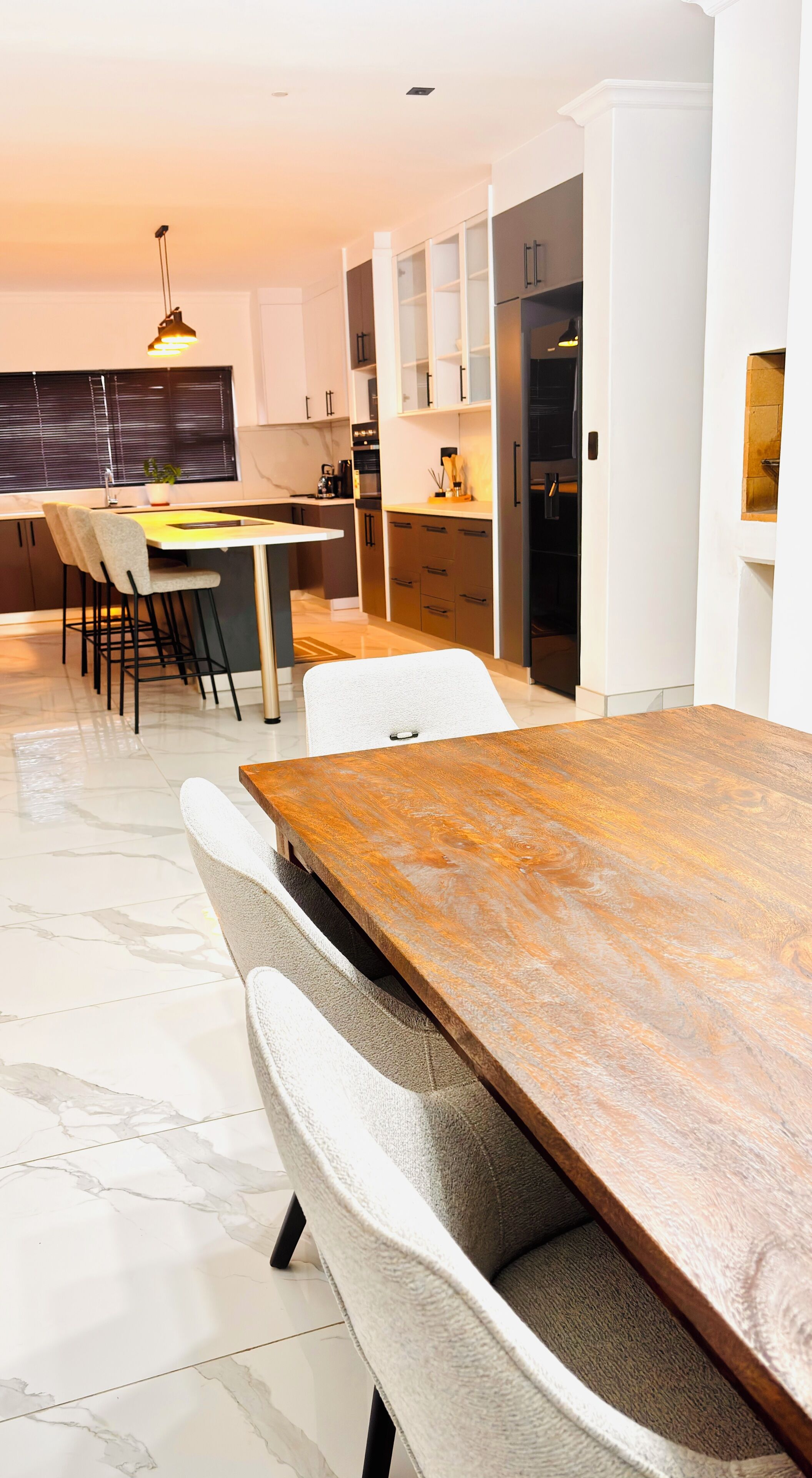 A modern kitchen with a dining area, featuring a marble floor, a wooden dining table, and contemporary furniture.