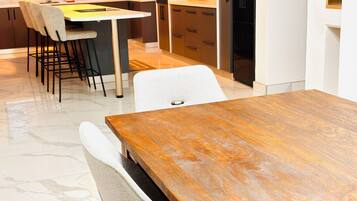 A modern kitchen with a dining area, featuring a marble floor, a wooden dining table, and contemporary furniture.