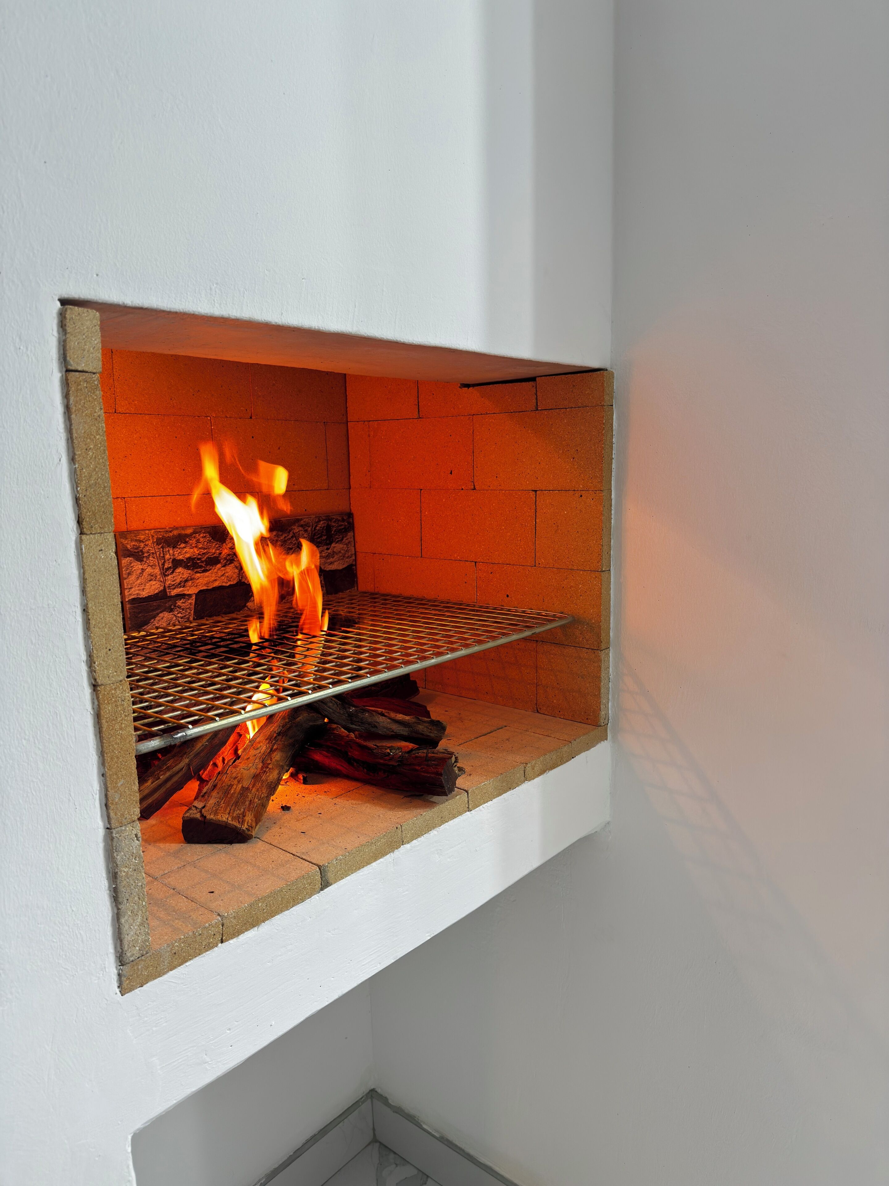 Una chimenea con rejilla metálica y leña encendida.